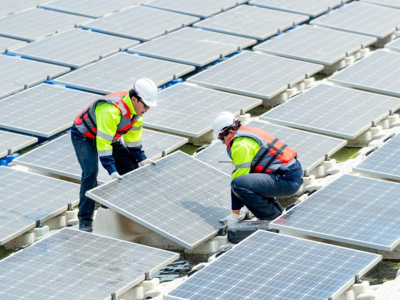 Side view of two technician workers help to install or set up solar panels over water reservoir