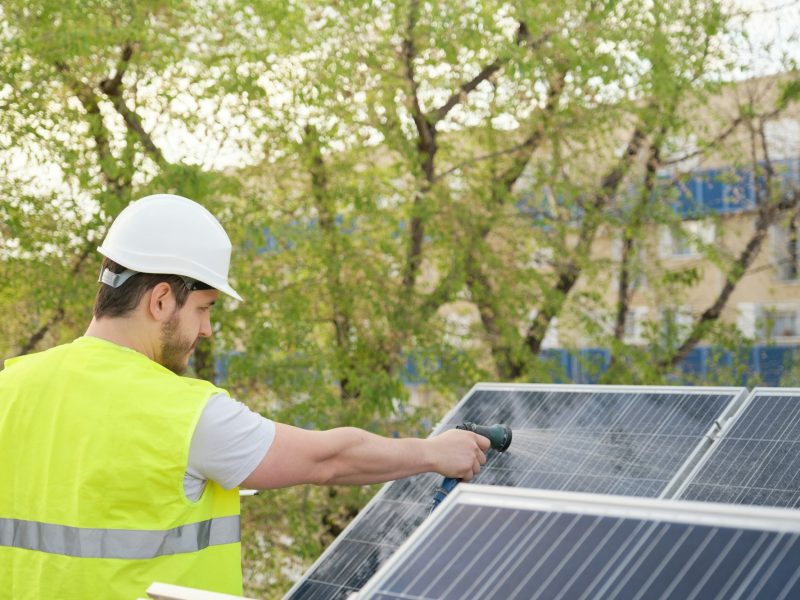 Technician cleaning solar panels with a hose.