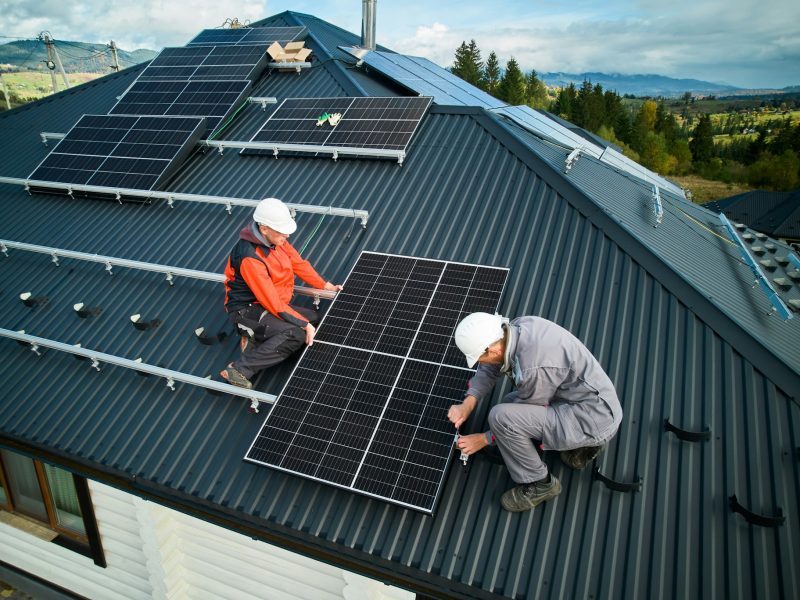 Technicians installing photovoltaic solar panels on roof of house.